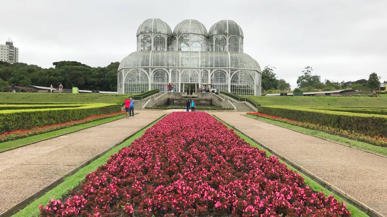 A imagem mostra a estufa principal do Jardim Botânico. Ela parece um castelo com três cúpulas de vidro