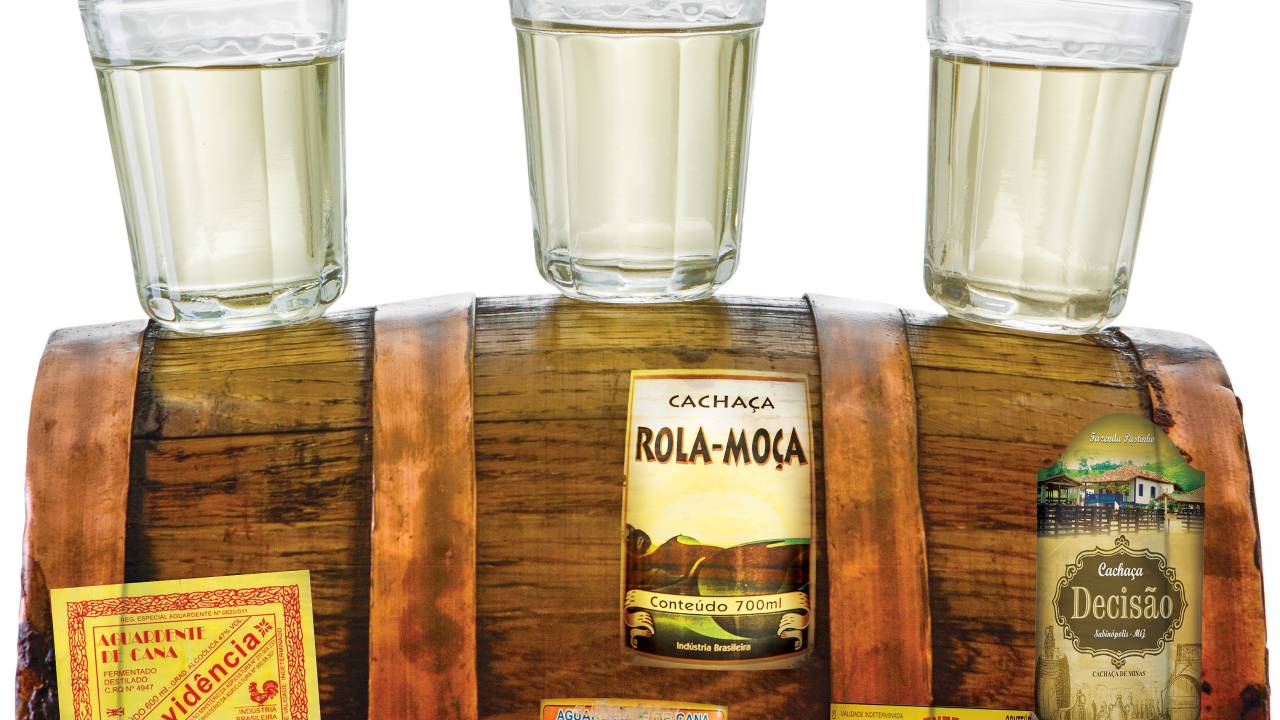 Copos de cachaça em cima de barril de pinga com rótulos de cachaça colados na madeira do barril