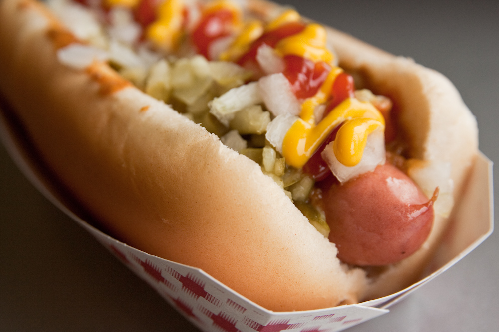 Cachorro quente com salsicha coberta de mostarda, ketchup e vinagrete em close up