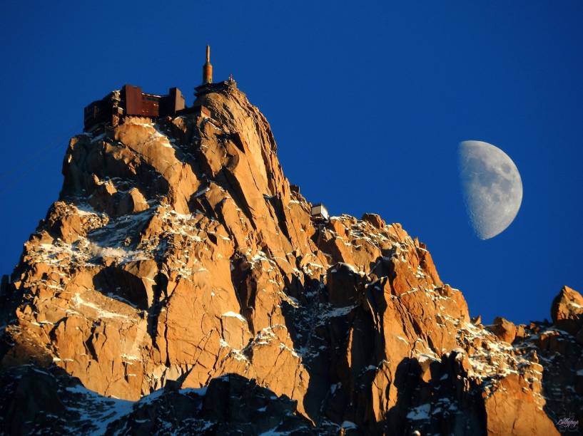 O topo do Mont Blanc, com a Lua ao fundo; o monte mais alto dos <a href="https://viajeaqui.abril.com.br/materias/esqui-e-vida-selvagem-na-francesa-chamonix" rel="Alpes Franceses" target="_blank">Alpes Franceses</a> fica em <a href="https://viajeaqui.abril.com.br/materias/esqui-e-vida-selvagem-na-francesa-chamonix" rel="Chamonix" target="_blank">Chamonix</a>, um dos destinos de esqui na região mais frequentados por brasileiros 