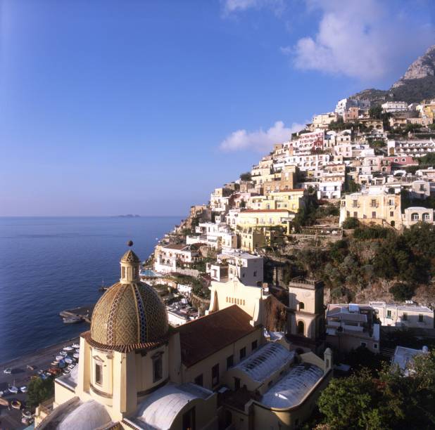 Vista da orla do vilarejo de <a href="https://viajeaqui.abril.com.br/cidades/italia-positano" rel="Positano">Positano</a>, na Costa Amalfitana, com a cúpula de cerâmica da Igreja Santa Maria Assunta em primeiro plano