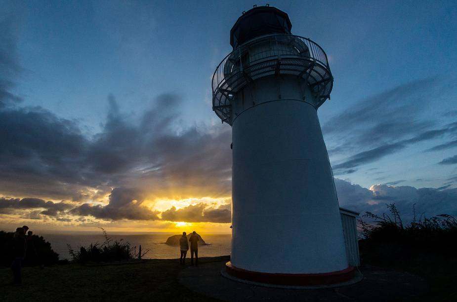 Turistas observam o pôr do sol a partir do farol de Gisborne Turistas observam o pôr do sol a partir do farol de Gisborne