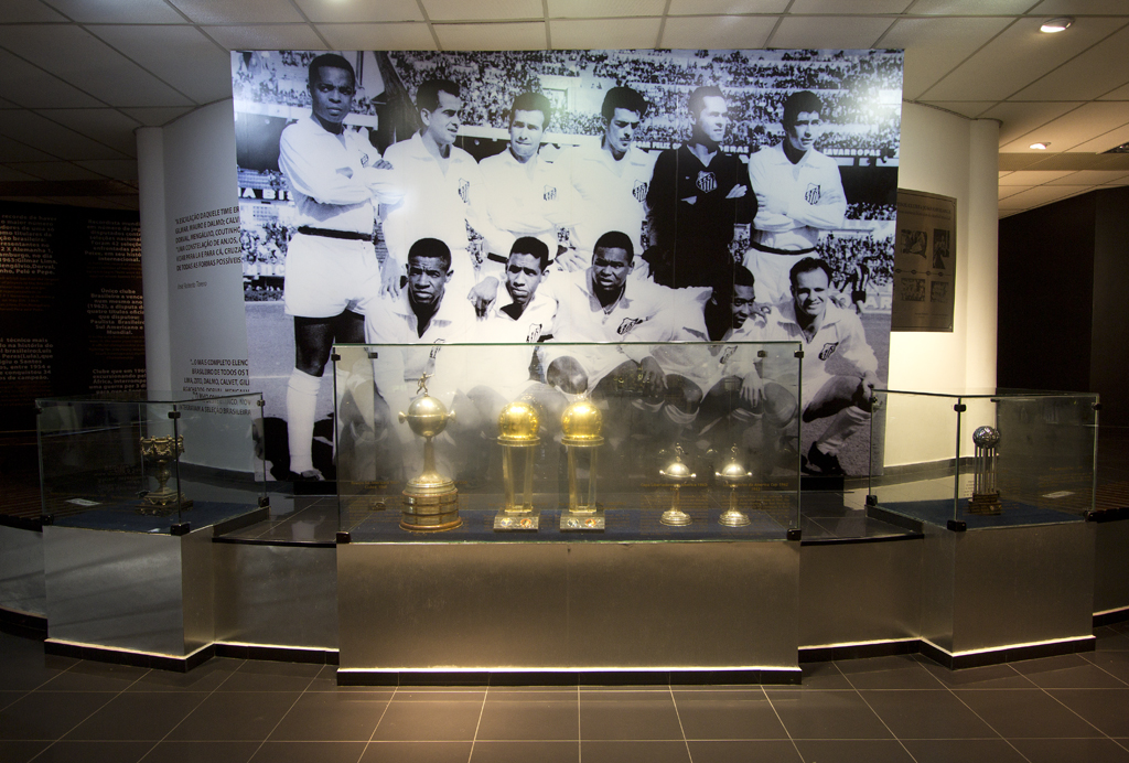 As ta&ccedil;as dos t&iacute;tulos mundiais do Santos e, ao fundo, a foto do time campe&atilde;o