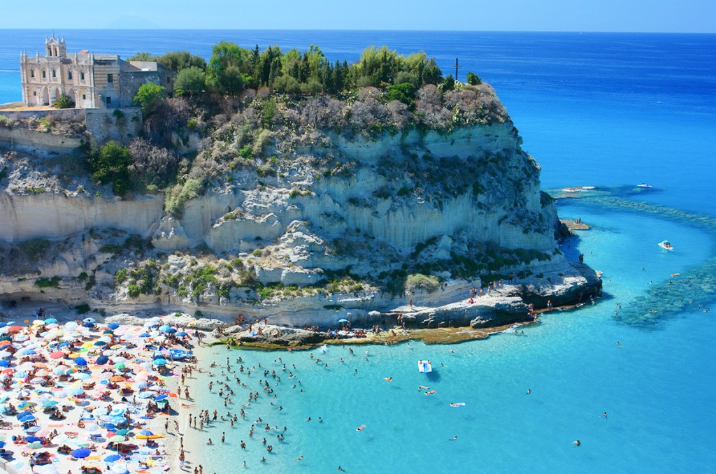 <strong>Praia de Tropea, Cal&aacute;bria, <a href="https://viajeaqui.abril.com.br/paises/italia" rel="It&aacute;lia" target="_self">It&aacute;lia</a>&nbsp;</strong>                Um precip&iacute;cio comp&otilde;e a paisagem do cen&aacute;rio, proporcionando uma bel&iacute;ssima vis&atilde;o ao visitante, sobretudo no p&ocirc;r do sol. Por aqui, as &aacute;guas cristalinas impressionam, convidando a passeios como o de pedalinho. O entorno da praia revela uma cidade antiga, repleta de constru&ccedil;&otilde;es hist&oacute;ricas. Por aqui, tamb&eacute;m h&aacute; muitos bons restaurantes de frutos do mar                <em><a href="https://www.booking.com/city/it/tropea.pt-br.html?sid=5b28d827ef00573fdd3b49a282e323ef;dcid=1?aid=332455&label=viagemabril-as-mais-belas-praias-do-mediterraneo" rel="Veja pre&ccedil;os de hot&eacute;is em Tropea no Booking.com" target="_blank">Veja pre&ccedil;os de hot&eacute;is em Tropea no Booking.com</a></em>