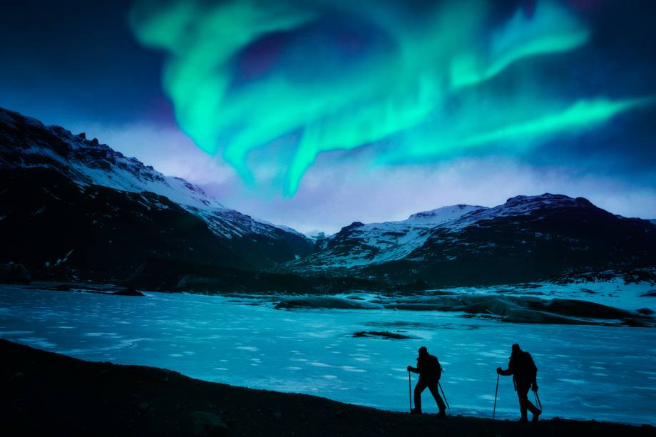 Alpinistas desbravando a Islândia, com as auroras boreais ao fundo Alpinistas desbravando a Islândia, com as auroras boreais ao fundo