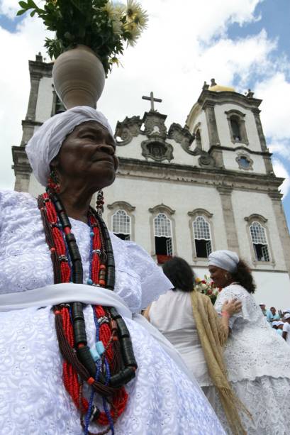 A <a href="https://viajeaqui.abril.com.br/estabelecimentos/br-ba-salvador-atracao-igreja-senhor-do-bonfim" rel="Igreja Senhor do Bonfim" target="_blank"><strong>Igreja Senhor do Bonfim</strong></a> leva o nome do padroeiro dos baianos e é também símbolo do sincretismo religioso na cidade. A tradição de lavar a escadaria e o adro começou com os escravos, como preparativo para a festa em homenagem ao santo, e é mantida até hoje pelas baianas do candomblé (à esq.). Outra marca sincrética é a famosa fitinha (à dir.): ninguém sai daqui sem amarrá-la no pulso ou no portão.