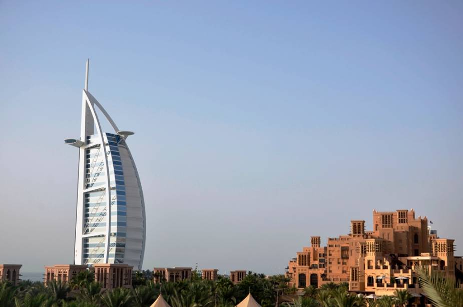 A modernidade das linhas do Burj al-Arab contrastando com a arquitetura tradicional do complexo de lojas e restaurantes de Madinat Jumeirah. Os edifícios têm aproximadamente a mesma idade