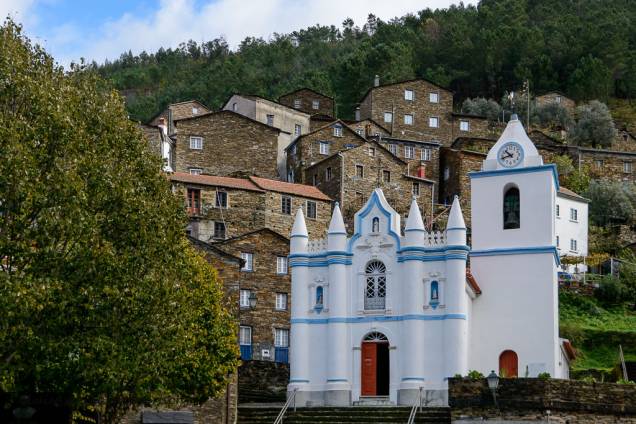 Aos pés da Serra do Açor, o pequeno povoado de <strong>Piodão </strong>ergue-se com casinhas de xisto e uma igreja pintada de branco que se destaca na paisagem. Ela é chamada de “Aldeia Presépio” e considerada uma das cidades mais típicas de Portugal Aos pés da Serra do Açor, o pequeno povoado de <strong>Piodão </strong>ergue-se com casinhas de xisto e uma igreja pintada de branco que se destaca na paisagem. Ela é chamada de “Aldeia Presépio” e considerada uma das cidades mais típicas de Portugal