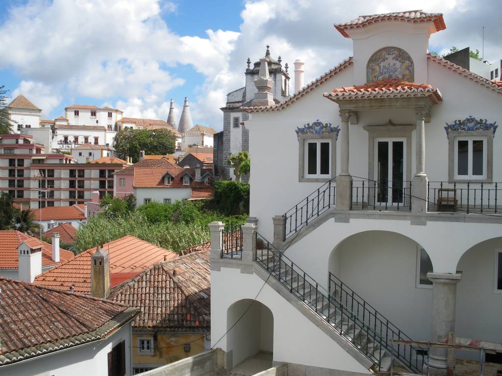 Se chegar &agrave; <strong>Sintra </strong>no come&ccedil;o da manh&atilde;, &eacute; poss&iacute;vel que voc&ecirc; v&aacute; encontrar a cidade coberta de neblina, com as chamin&eacute;s do Pal&aacute;cio de Sintra &agrave; mostra l&aacute; no alto. Com o passar do dia, a neblina se dissipa e revela as ab&oacute;badas arredondadas do <strong>Pal&aacute;cio da Pena</strong>, as casas coloridas e a rica natureza ao redor da cidade. Devido &agrave; sua proximidade com Lisboa, Sintra &eacute; uma boa alternativa para um bate-e-volta &ndash; seja de carro ou de trem (que os portugueses chamam de comboio)