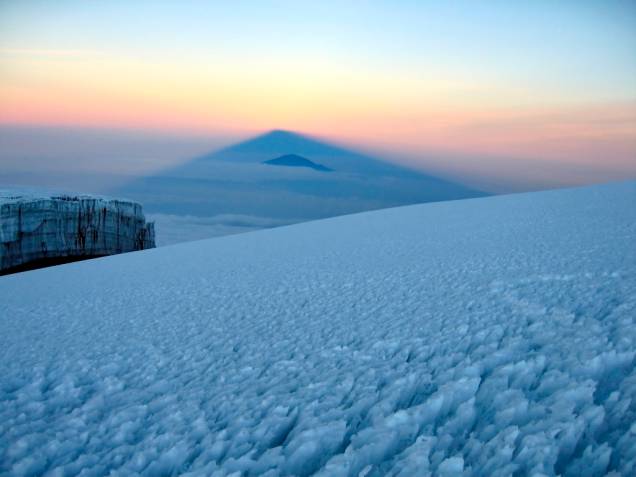 Muitos escaladores que estão no cume do Kilimanjaro acordam cedo para ver a sombra do cone vulcânico esparramar-se sobre as planícies (ou nuvens) ao seu redor Muitos escaladores que estão no cume do Kilimanjaro acordam cedo para ver a sombra do cone vulcânico esparramar-se sobre as planícies (ou nuvens) ao seu redor