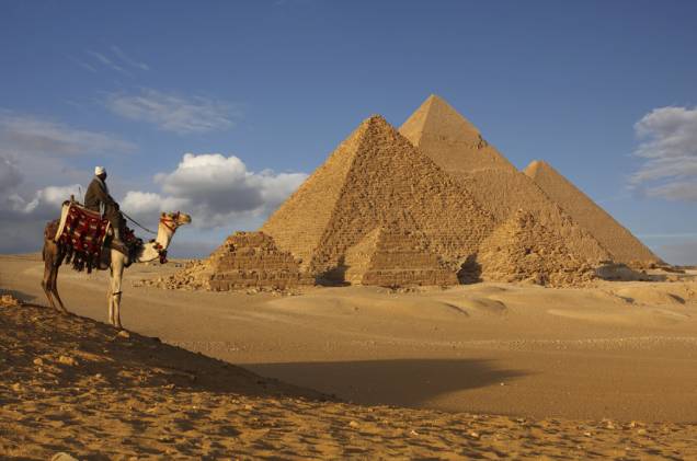 Beduíno e dromedário no platô de Gizé. Aos visitante, atenção, as pirâmides estão coladas aos subúrbios da cidade do Cairo Beduíno e dromedário no platô de Gizé. Aos visitante, atenção, as pirâmides estão coladas aos subúrbios da cidade do Cairo