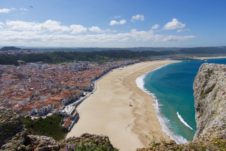 Nazaré, praticamente dependurada sobre um penhasco na costa, passou a chamar atenção nos últimos anos pelas ondas gigantes, ou maiores ondas do mundo, e sua repercussão na mídia. A temporada das ondas grandes acontece nos meses frios, entre outubro e janeiro (o espetáculo pode ser visto em segurança de um mirante). A vibe da vila reúne surfistas corajosos (ou insanos?) e tradições antigas. A mais conhecida são as sete saias vestidas pelas nazarenas.  <em><a href="https://www.booking.com/searchresults.pt-br.html?aid=332455&sid=605c56653290b80351df808102ac423d&sb=1&src=searchresults&src_elem=sb&error_url=https%3A%2F%2Fwww.booking.com%2Fsearchresults.pt-br.html%3Faid%3D332455%3Bsid%3D605c56653290b80351df808102ac423d%3Bcity%3D-2176842%3Bclass_interval%3D1%3Bdest_id%3D-2170835%3Bdest_type%3Dcity%3Bdtdisc%3D0%3Bfrom_sf%3D1%3Bgroup_adults%3D2%3Bgroup_children%3D0%3Binac%3D0%3Bindex_postcard%3D0%3Blabel_click%3Dundef%3Bno_rooms%3D1%3Boffset%3D0%3Bpostcard%3D0%3Braw_dest_type%3Dcity%3Broom1%3DA%252CA%3Bsb_price_type%3Dtotal%3Bsearch_selected%3D1%3Bsrc%3Dsearchresults%3Bsrc_elem%3Dsb%3Bss%3D%25C3%2593bidos%252C%2520Regi%25C3%25A3o%2520do%2520Centro%252C%2520Portugal%3Bss_all%3D0%3Bss_raw%3D%25C3%2593bidos%3Bssb%3Dempty%3Bsshis%3D0%3Bssne_untouched%3DSintra%26%3B&ss=Nazar%C3%A9%2C+Regi%C3%A3o+do+Centro%2C+Portugal&ssne=%C3%93bidos&ssne_untouched=%C3%93bidos&city=-2170835&checkin_monthday=&checkin_month=&checkin_year=&checkout_monthday=&checkout_month=&checkout_year=&group_adults=2&group_children=0&no_rooms=1&from_sf=1&ss_raw=Nazar%C3%A9&ac_position=0&ac_langcode=xb&dest_id=-2170637&dest_type=city&place_id_lat=39.60291&place_id_lon=-9.07016&search_pageview_id=ca727c10d50802ae&search_selected=true&search_pageview_id=ca727c10d50802ae&ac_suggestion_list_length=5&ac_suggestion_theme_list_length=0" target="_blank" rel="noopener">Busque hospedagens em Nazaré</a></em>