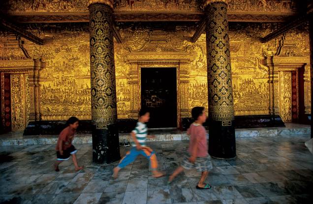 Acostumados com o magnífico cenário, meninos passam com pressa na frente dos muros dourados de Wat Mai, templo do século 18 ornamentado com cenas detalhadas da vida de Buda. A designação de Patrimônio da Humanidade abrange todo o vilarejo de Luang Prabang, uma antiga capital real Acostumados com o magnífico cenário, meninos passam com pressa na frente dos muros dourados de Wat Mai, templo do século 18 ornamentado com cenas detalhadas da vida de Buda. A designação de Patrimônio da Humanidade abrange todo o vilarejo de Luang Prabang, uma antiga capital real