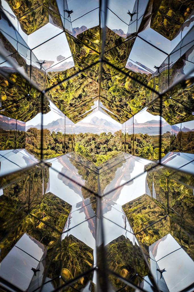 A vista da paisagem de Inhotim - árvores e céu ensolarado - por meio de uma espécie de caleidoscópio gigante de vidro, que reflete a vista diversas vezes