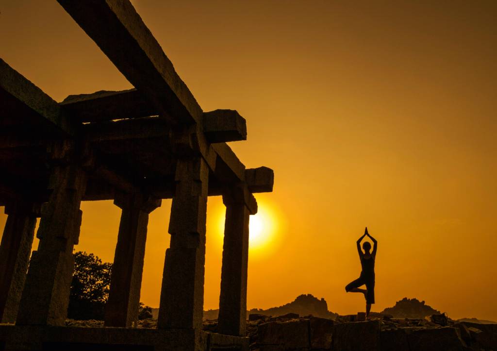 Ioga, Índia, Kerala Mulher faz pose de ioga ao lado de uma construção aparentemente abandonada. Ela está contra o pôr-do-sol, de forma que suas feições não estejam visíveis