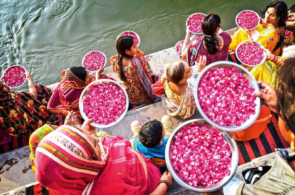 Ganges, Índia Em degraus de pedra localizados na margem do Ganges, miulheres se reúnem com bacias de pétalas de flores para jogá-las no rio, em oferenda