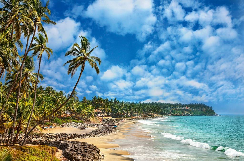 Varkala, Kerala, Índia praia quase vazia de sinais humanos embaixo de um céu sem nuvens. Não há muita areia e os coqueiros existem em abundância