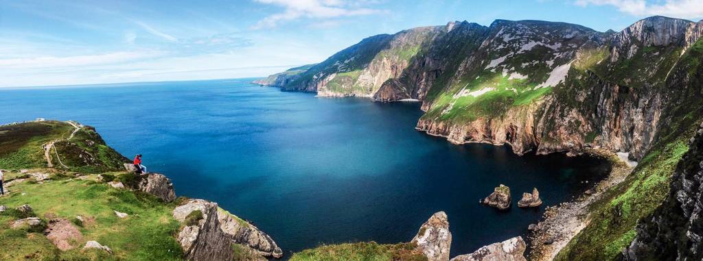 Em primeiro plano, montanhas à beira d'água formam uma baía natural. Ao fundo, o horizonte marítimo