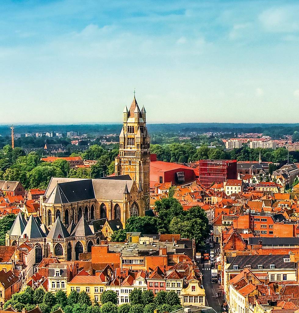 A torre da catedral se eleva acima dos outros prédios e casas em meio às ruas de Bruges