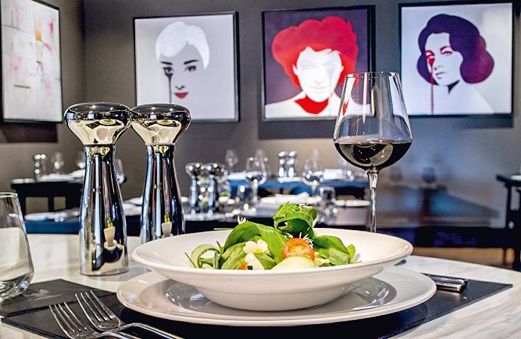 Prato do Blas Restaurant, do Twr y Felin Hotel, em Pembrokeshire, País de Gales Prato de salada em restaurante requintado, cercado por talheres lustrosos e quadros minimalistas de mulheres