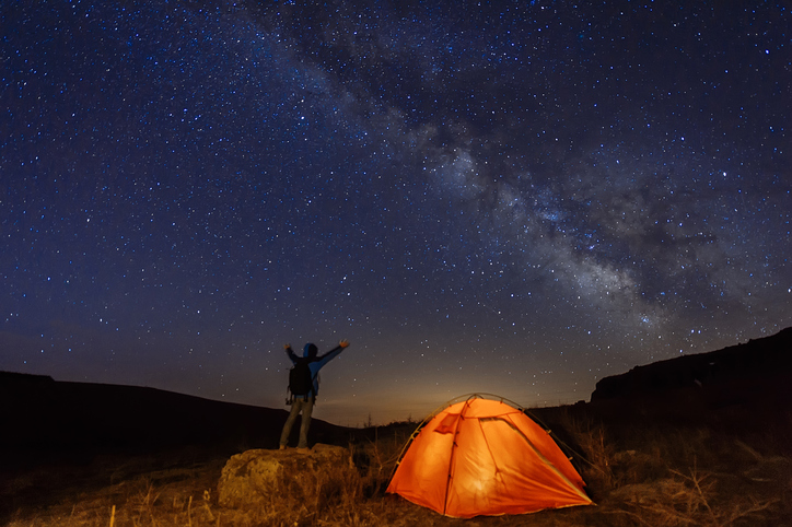 Homem e sua barraca em uma noite estrelada