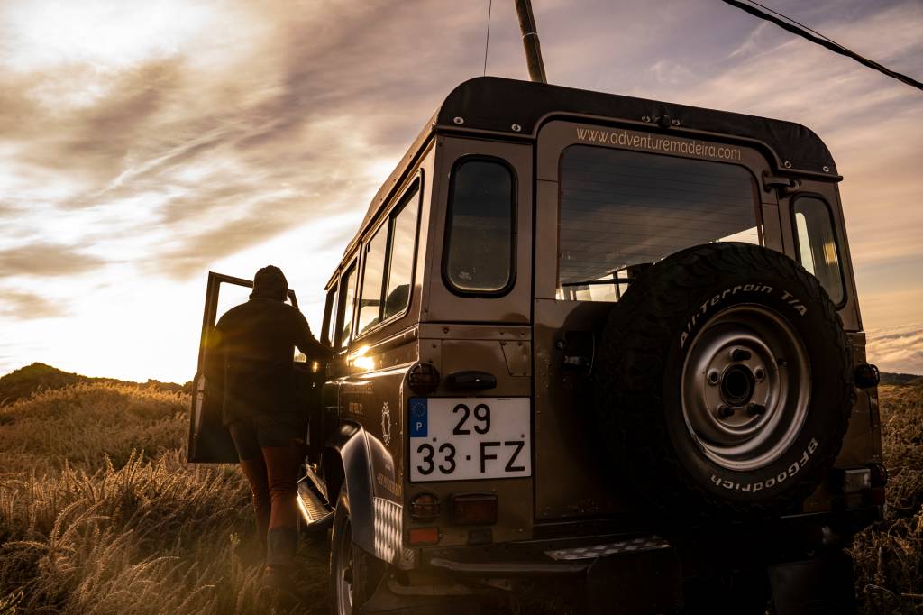 Jipe estacionado no alto da montanha, com o motorista do lado de fora a observar a paisagem, na Ilha da Madeira