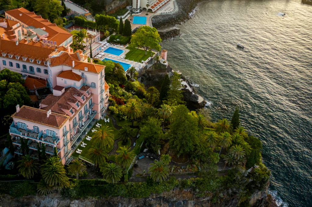 Vista aérea do hotel Reid's Palace, com o palacete rosa, duas piscinas e o jardim botânico debruçados sobre o mar