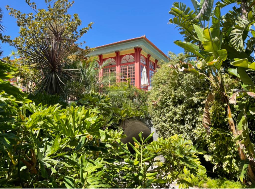 Jardim tropical com plantas exuberantes e uma construção de ares orientais ao fundo, com colunas vermelhas