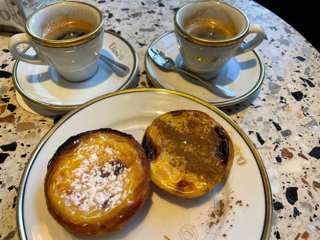 Dois doces redondos e amarelos, cobertos de açúcar e canela, ao lado de duas xícaras de café