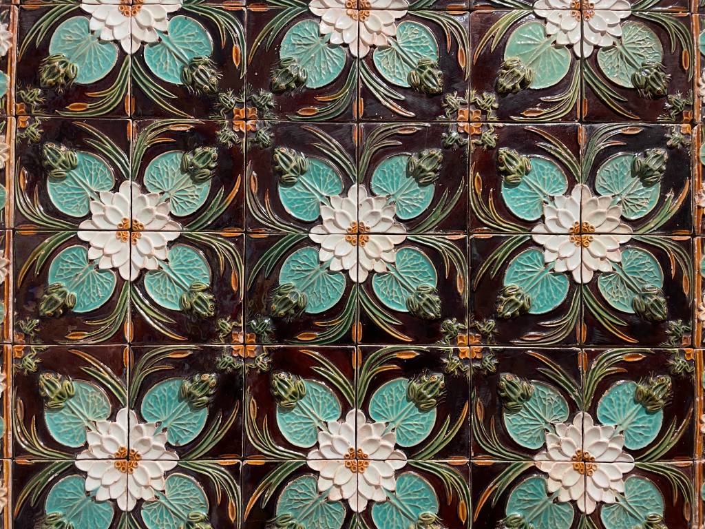 Detalhe de uma composição de azulejos que retratam flores brancas cercadas de folhas em diferentes tons de verde, com pequenos sapos nas pontas