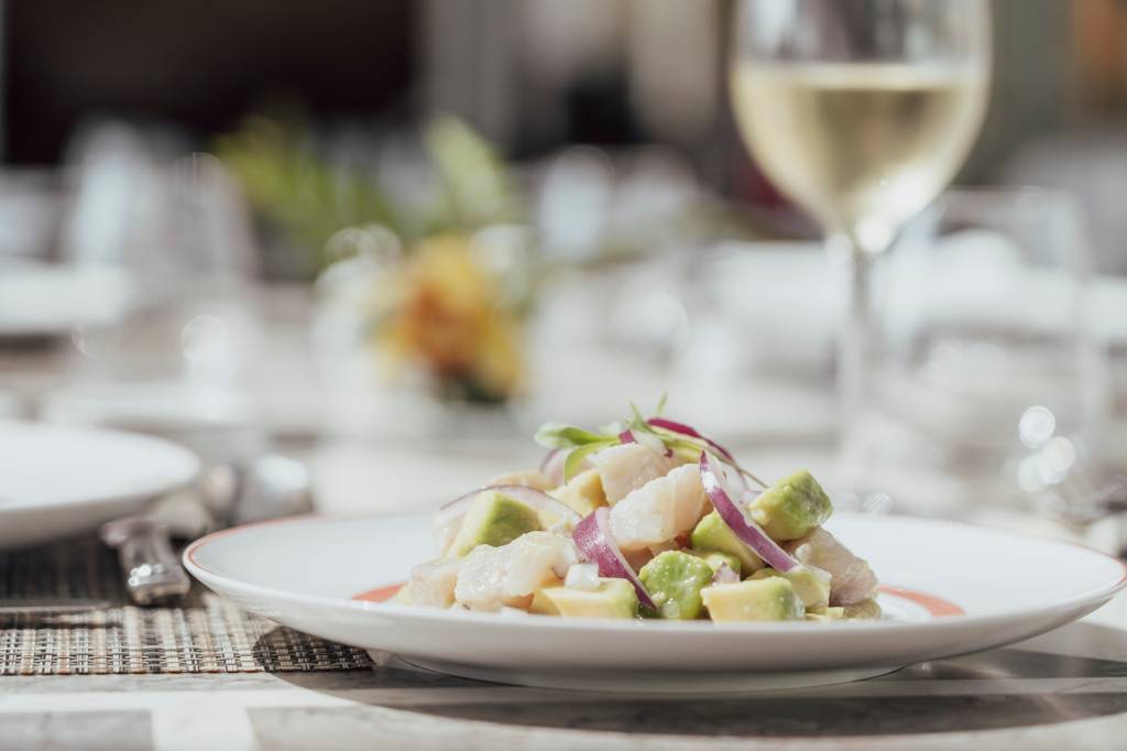 Prato de ceviche com uma taça de vinho branco ao lado