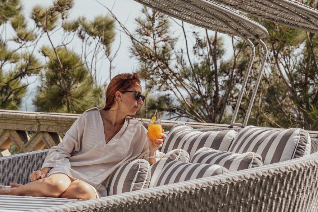 Mulher com um copo de suco de laranja na mão, em uma espreguiçadeira