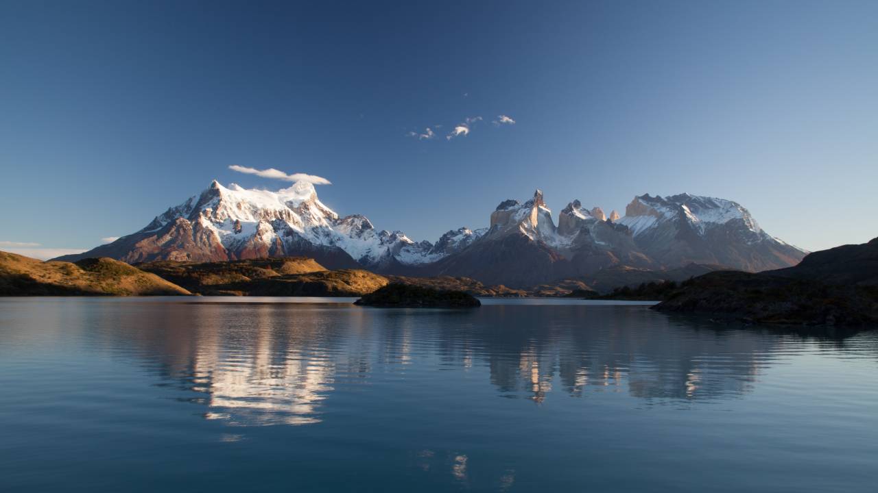 A imagem mostra uma formação montanhosa nevada atrás de um lago