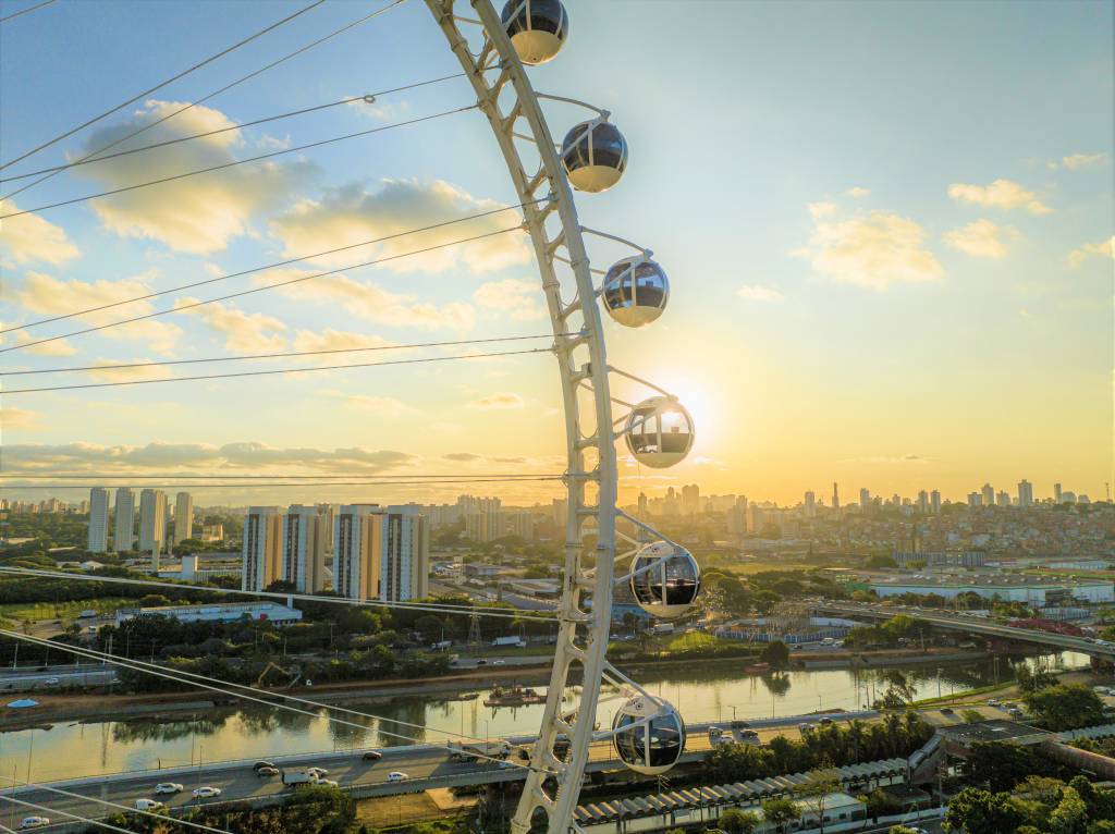 Cabines da Roda Rico São Paulo A fotografia colorida mostra as cabines de uma roda-gigante no fim do dia, com o céu azul e amarelo