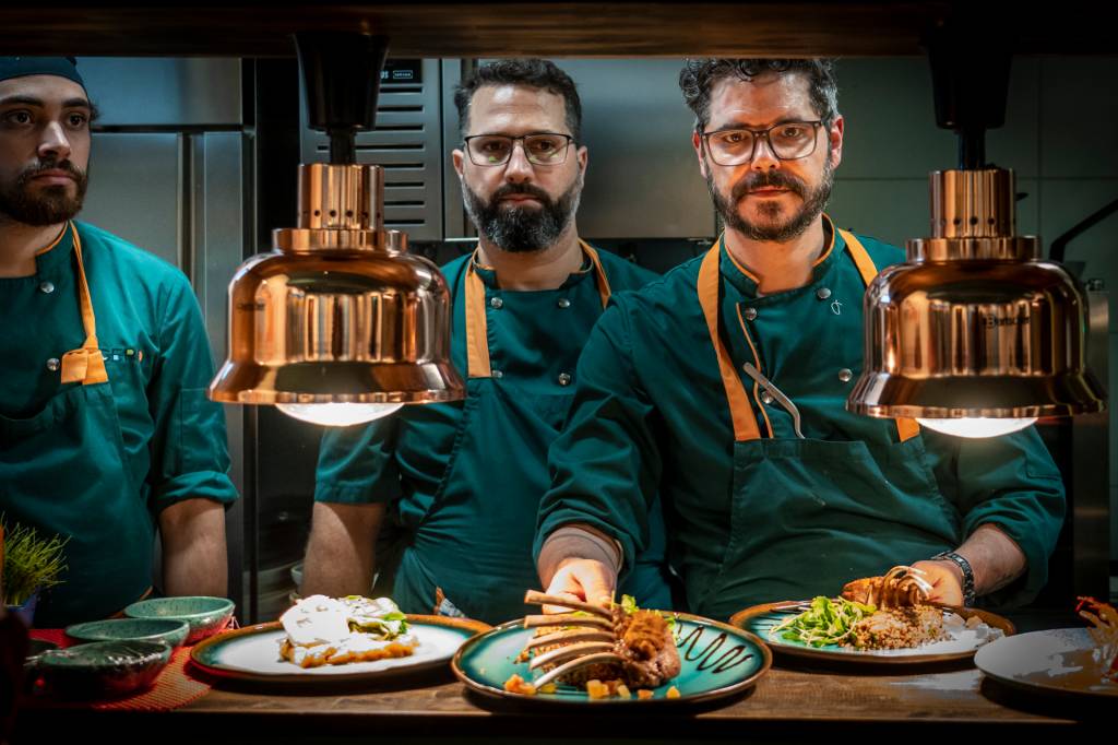 11 Janela da cozinha do restaurante onde se vê três cozinheiros vestidos de verde, mostrando os pratos