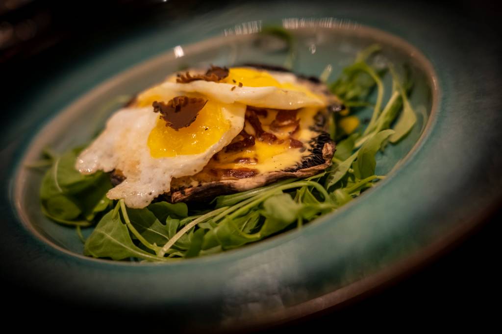 7 Prato do restaurante onde se vê uma base de rúcula e, sobre ela, um cogumelo com pedacinhos de presunto e fatias de trufas frescas
