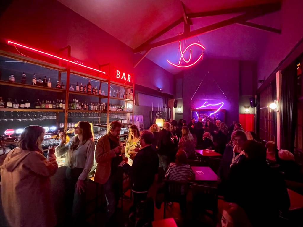 Bar com pessoas ao balcão e decoração de neon nas paredes