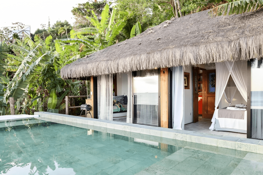 A imagem mostra uma piscina em frente a uma cabana com portas de vidro