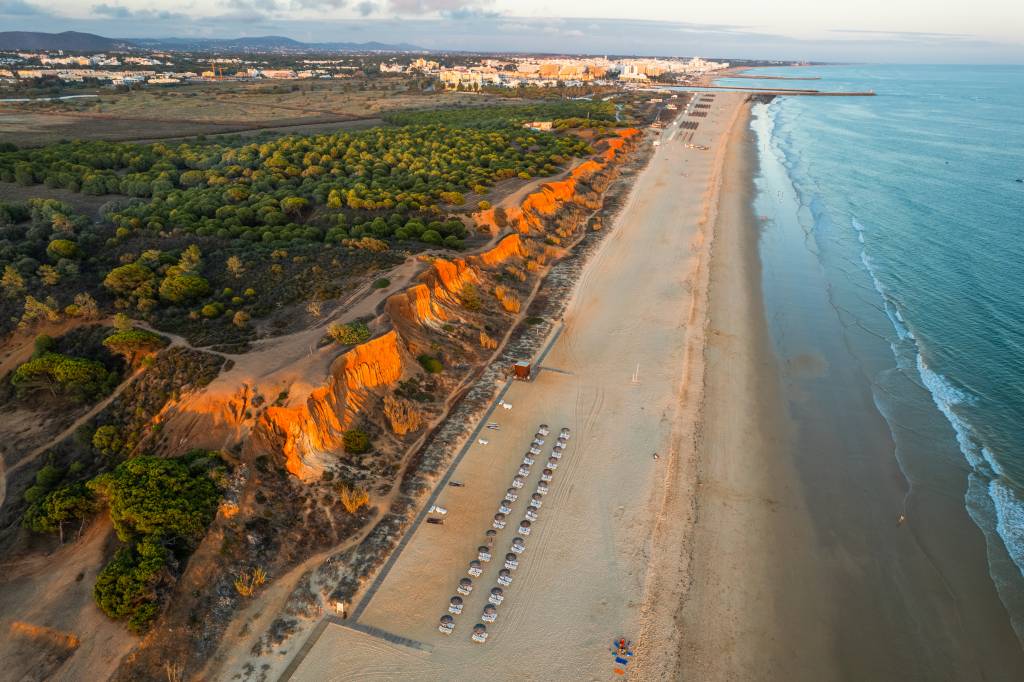 Fotografia colorida aérea mostra a praia eleira a melhor do mundo do alto, destacando suas falésias coloridas cobertas por pinheiros