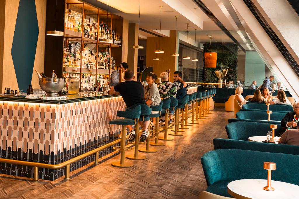 Bar do hotel com pessoas sentadas em poltronas de veludo azul