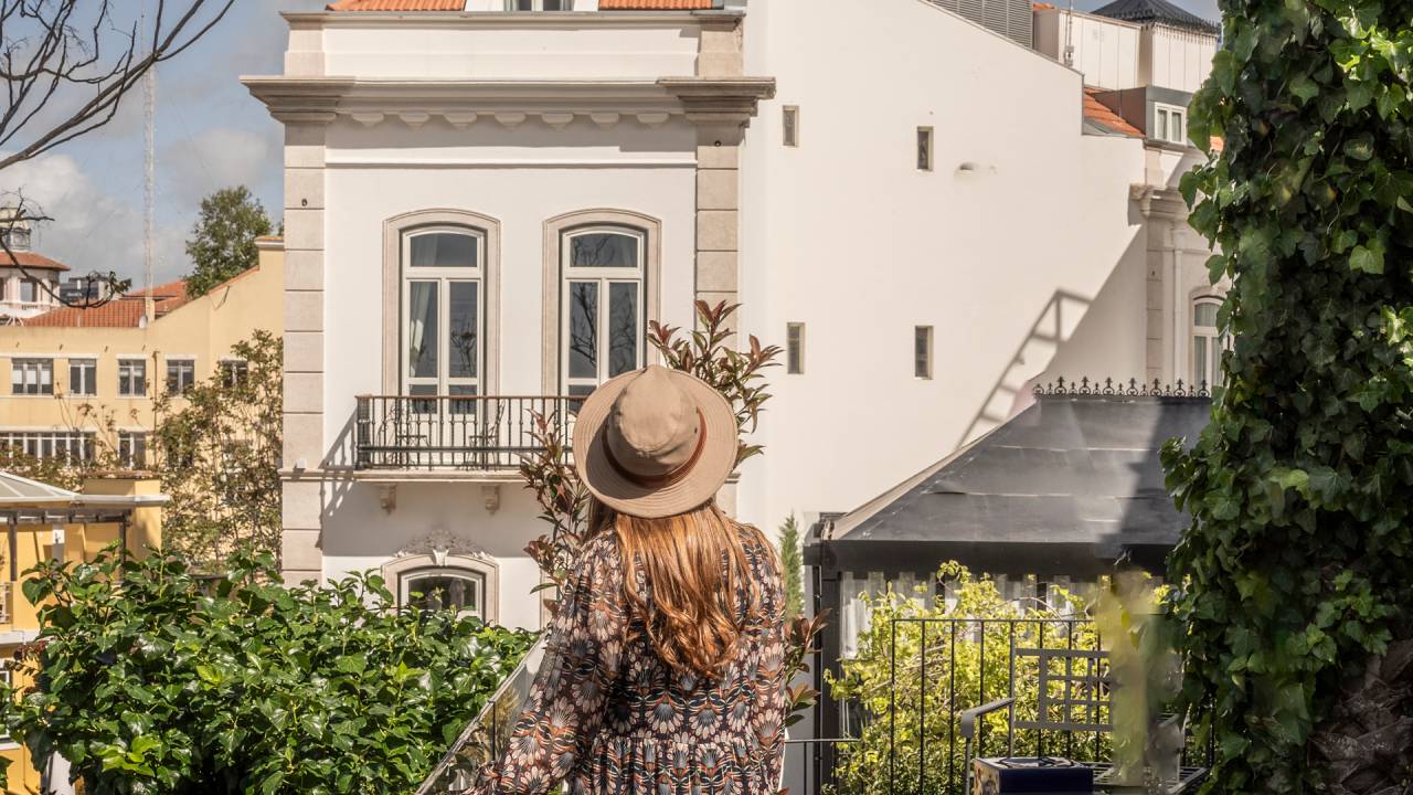A imagem mostra uma mulher de chapéu no jardim do hotel, de frente para edifícios históricos tipicamente lisboetas
