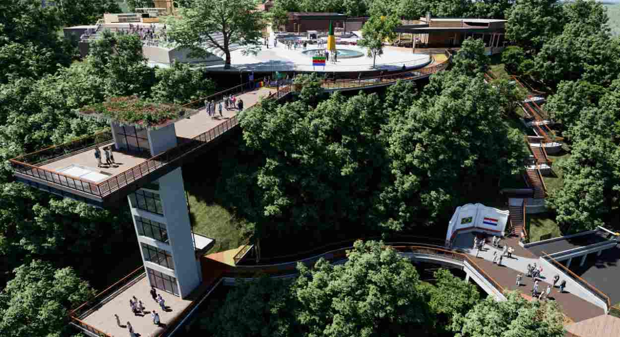 Vista aérea de um complexo turístico moderno em meio a uma densa floresta, com passarelas elevadas e edifícios de vidro. Pessoas caminham pelas passarelas e plataformas de observação, algumas com telhados verdes. Há uma praça circular com um monumento e bandeiras coloridas, além de escadarias que descem pela encosta.