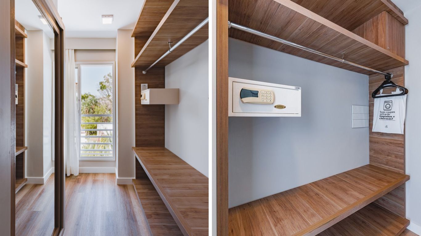 Um closet moderno com piso e prateleiras de madeira clara, paredes brancas e um espelho de corpo inteiro. H&aacute; um cofre digital branco embutido e um saco de lavanderia pendurado em um cabide. Ao fundo, uma janela com vista para &aacute;rvores e um c&eacute;u azul