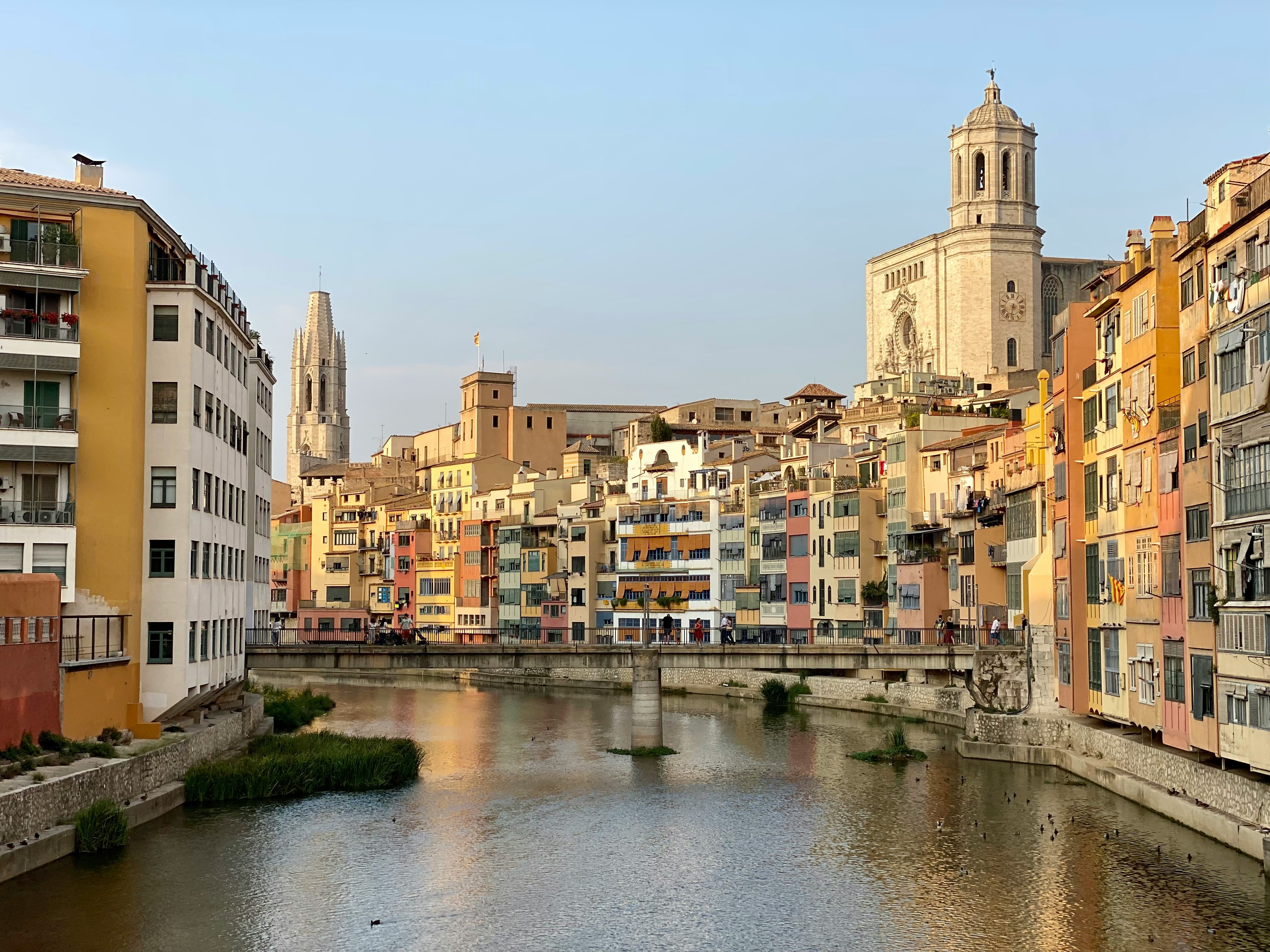 Rio com águas calmas e reflexos, ladeado por edifícios coloridos de vários andares. Ao fundo, torres de igrejas históricas se destacam no céu claro.